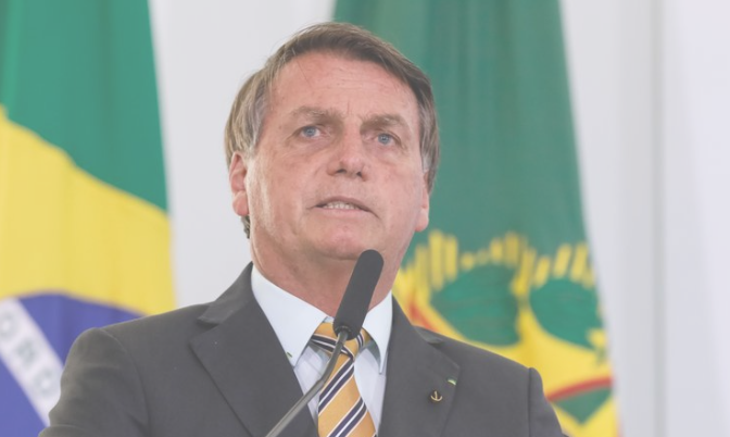 bolsonaro com bandeira 1 Governo é a favor de aquisição de 33 milhões de doses da AstraZeneca por empresas brasileiras; Bolsonaro defende metade delas doadas para o SUS